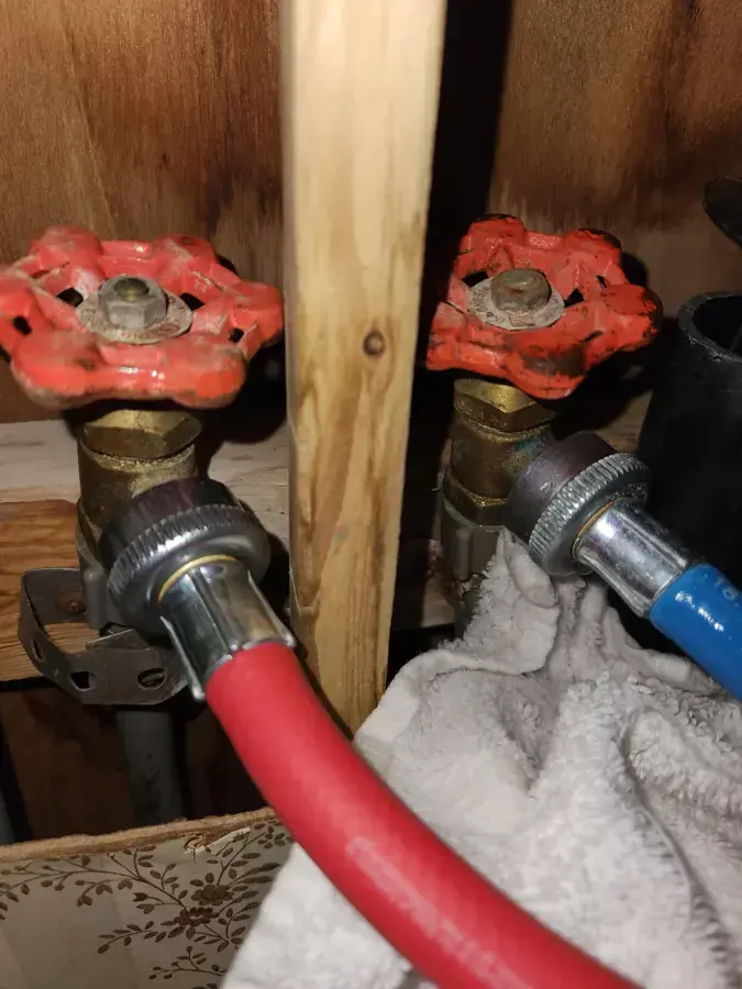 Washer supply hoses on red shutoff valves with a towel catching a leak in a Wilmington laundry