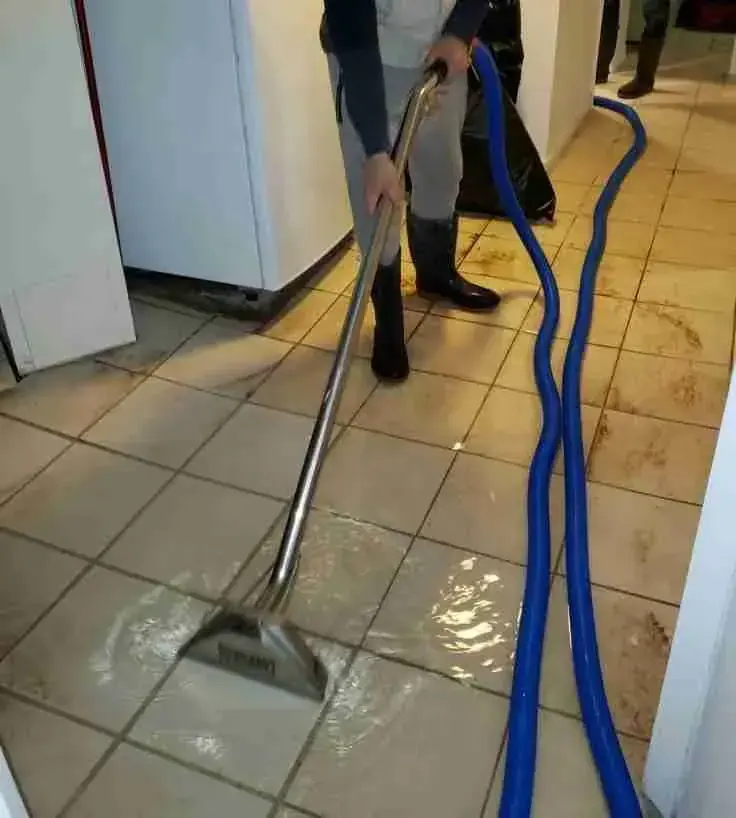 Technician running an extraction wand over standing water on a tile floor in a Wilmington home